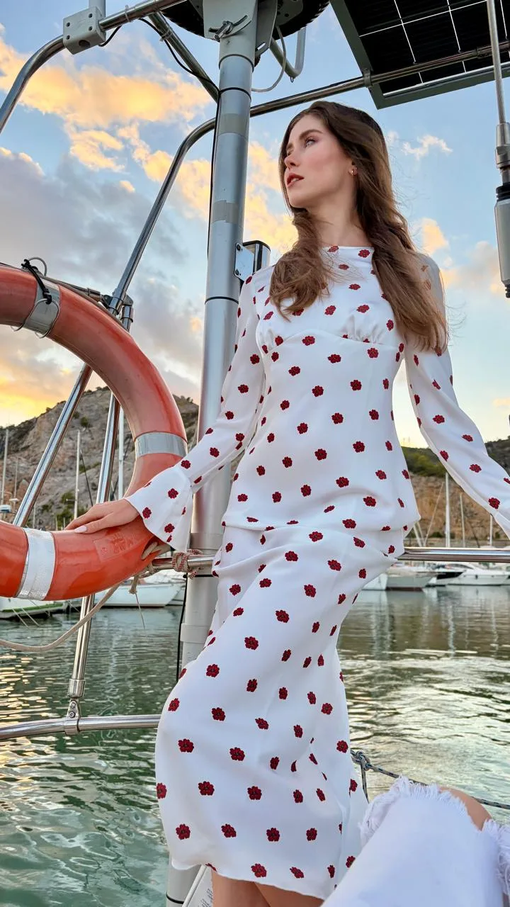 Modelo con vestido blanco posando en cubierta del velero junto al salvavidas, con el cielo del atardecer en Port Garraf