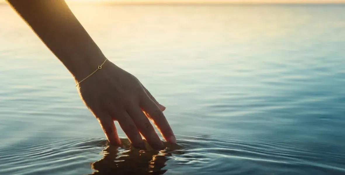 Mano tocando el agua del mar en una despedida íntima
